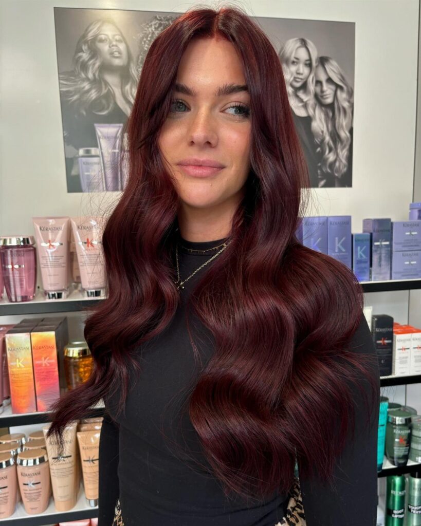 Woman with long glossy burgundy waves standing in a salon