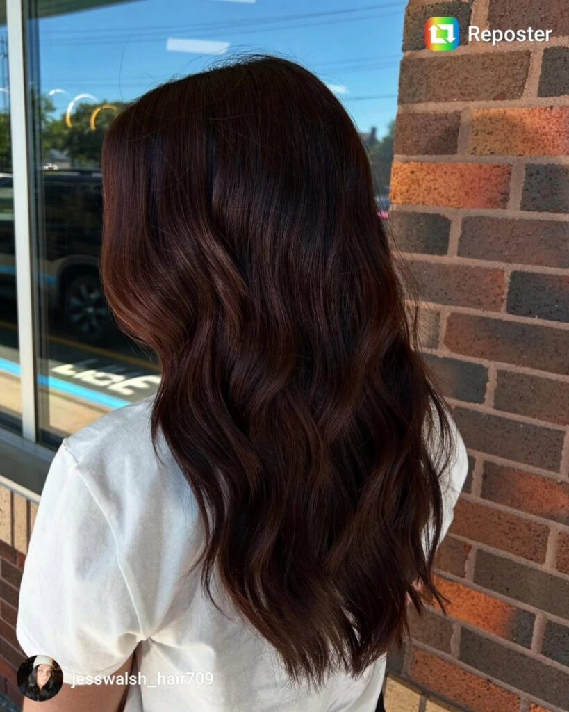 Long wavy chestnut brown hair falls over a white top