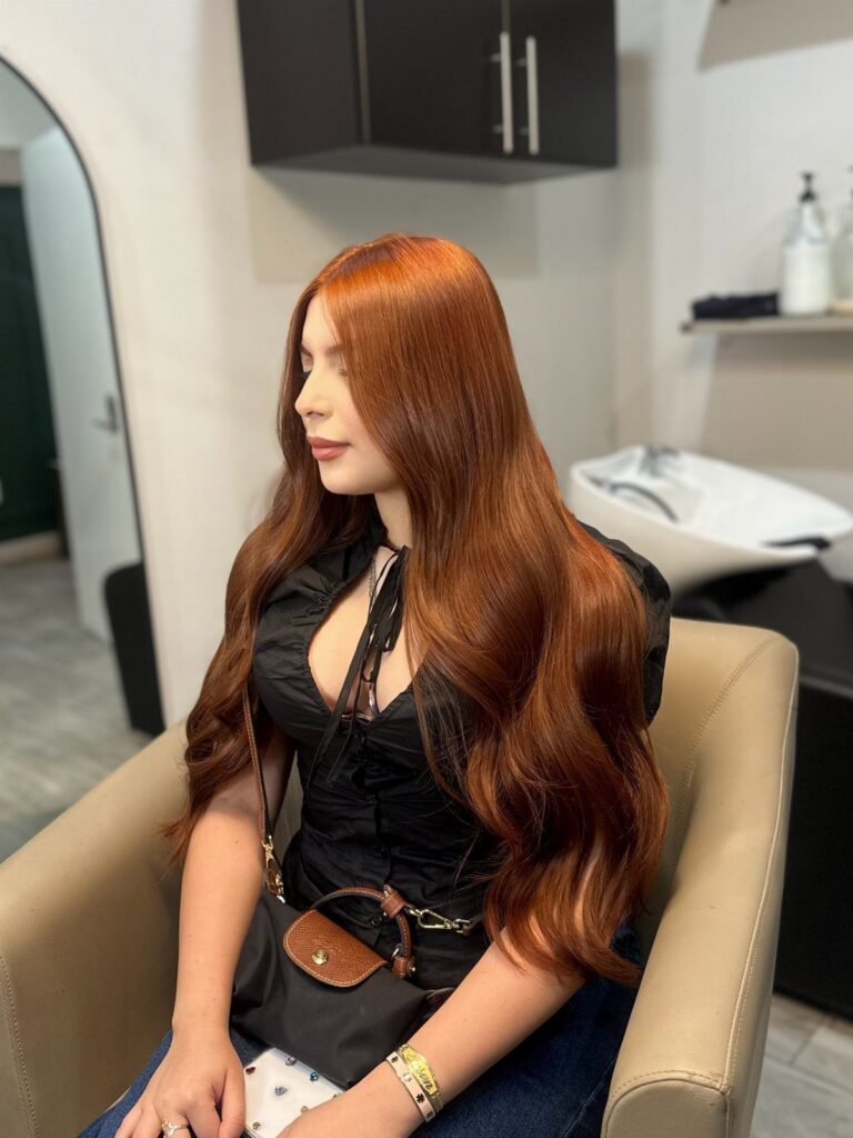 Woman displaying long glossy copper hair in loose waves at a salon