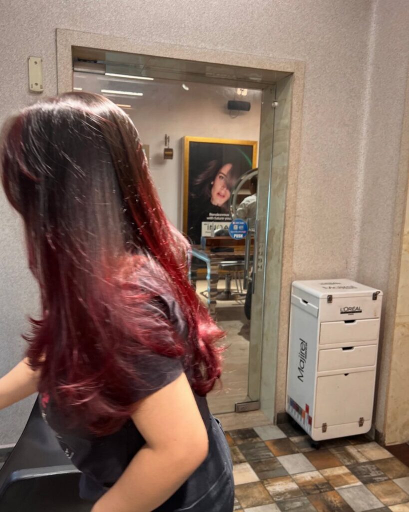 Long, wavy dark red hair shown from behind in a salon mirror