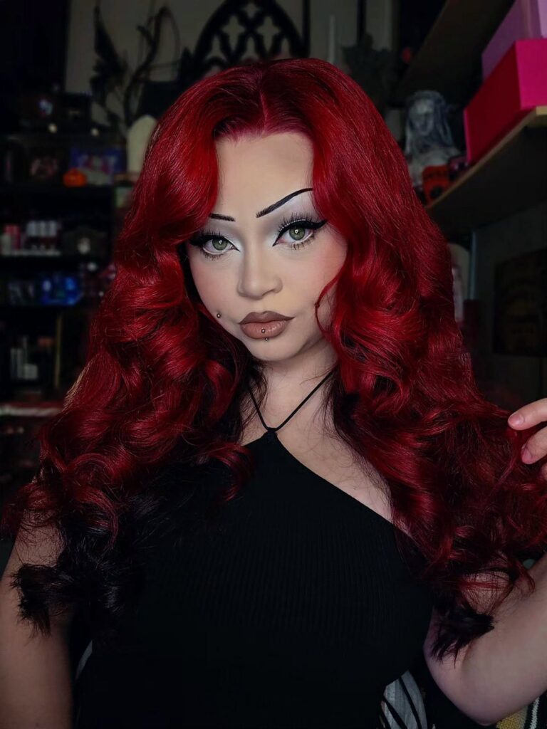Woman with long, vivid red dyed hair posing in a black top