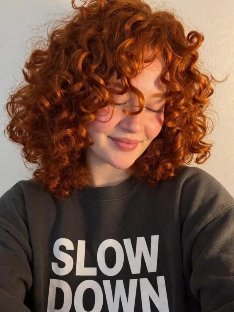 Woman with voluminous curly ginger-red hair wearing a dark lettered sweatshirt