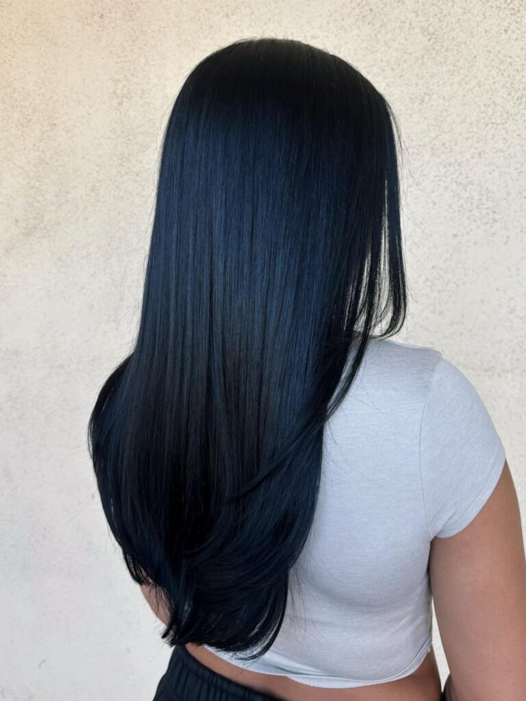 Long, glossy jet-black hair falling down the back of a person in a white top