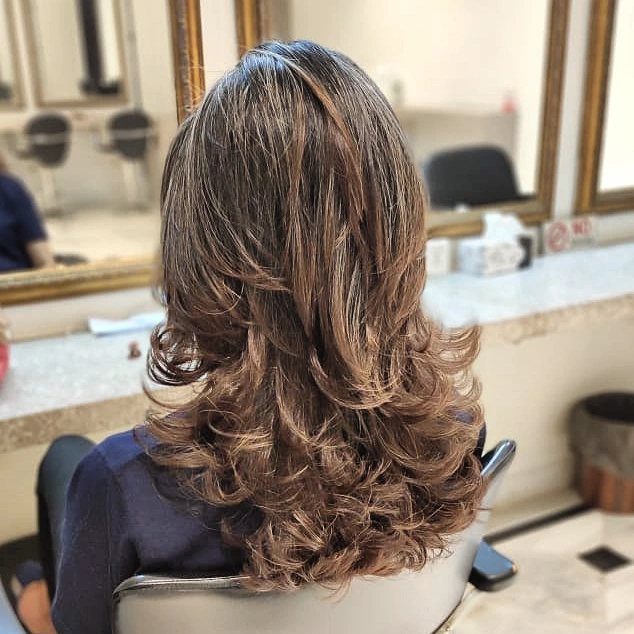 Medium-length brown layered haircut with curled ends shown from behind in a salon