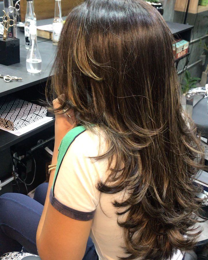 Long brown layered haircut with cascading curls shown from behind in a salon