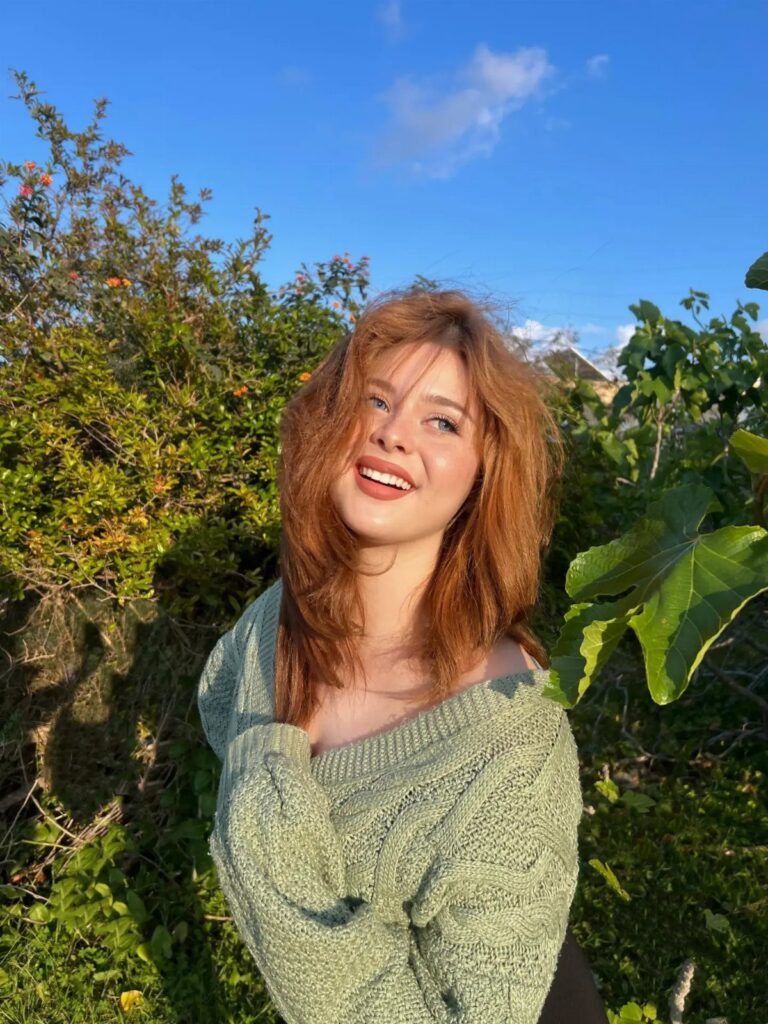 Smiling woman with natural red hair posing in a sunny leafy garden