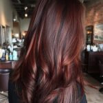 Glossy mahogany hair falls in long, layered waves with reddish brown shine