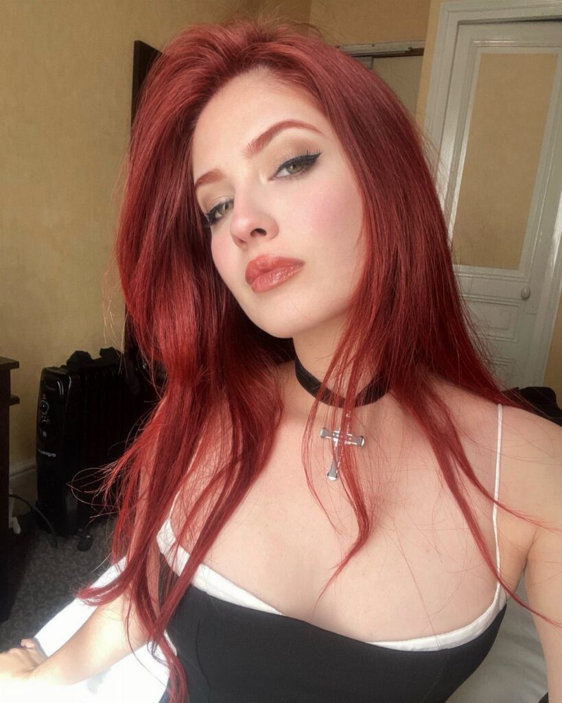 Person with long vivid red hair posing indoors in a black-and-white top
